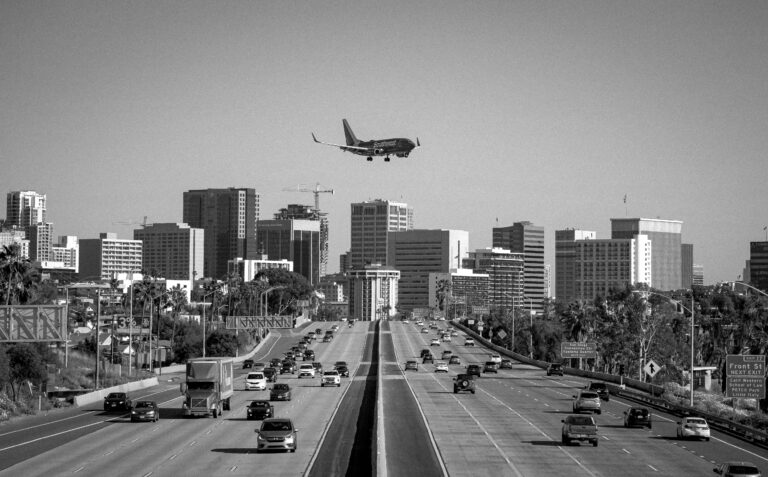 A commercial airplane flying over a busy city highway with multiple vehicles below.